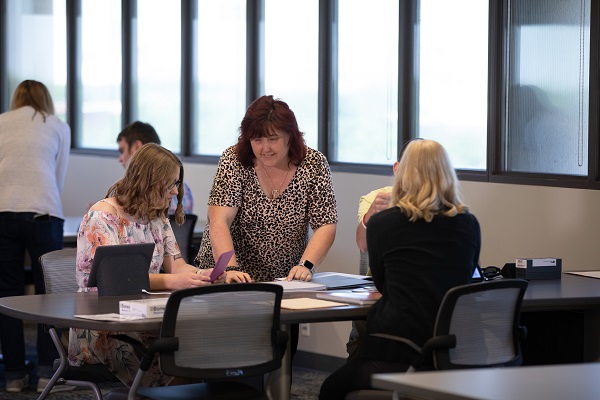 A woman who is blind instructing other female employees at work at a table