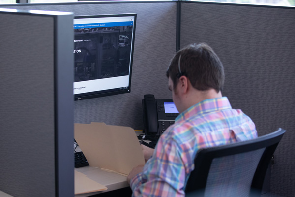 A male employee working is his cubicle in front of his computer and headset