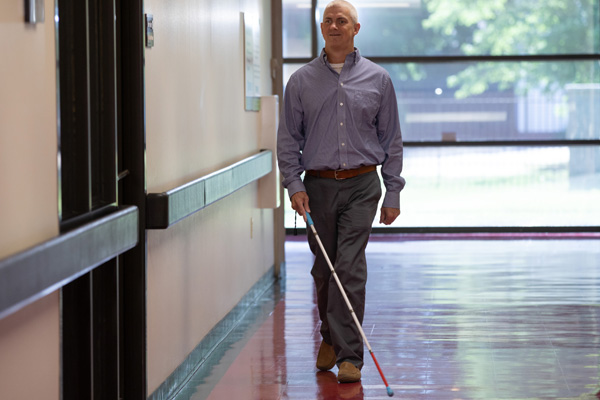 Man who is blind walking with a white cane down the hallway at work