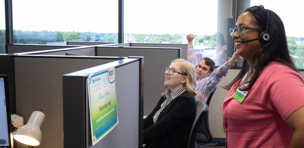 Three customer contact co-workers chatting at their cubicles.