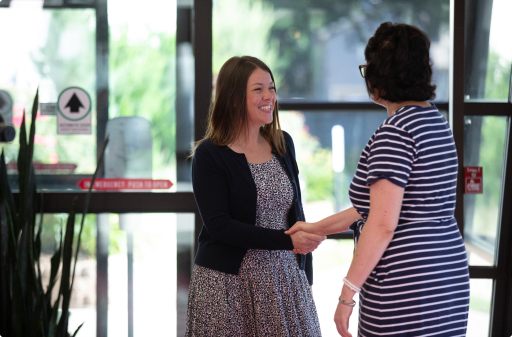 Two women in a hallway smiling at each other and shaking hands.