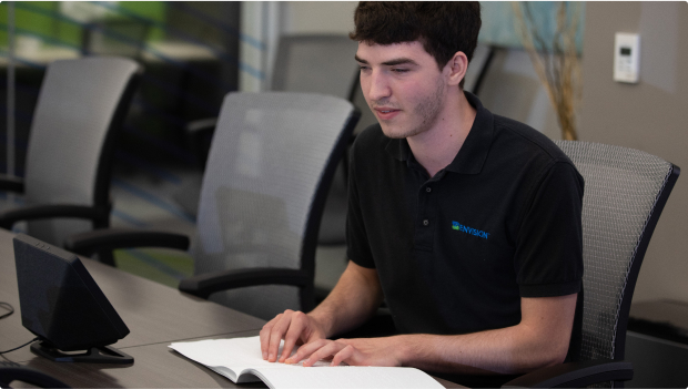 A young man reading from a book with Braille.