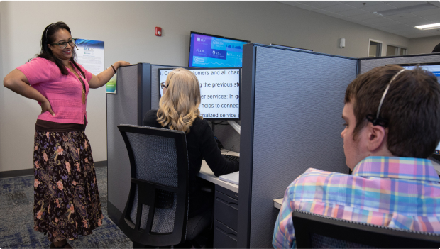 A supervisor checking in on her employees at their desk.