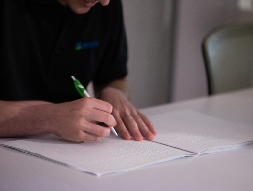 Male who is blind at work reading braille and has a pen in his hand