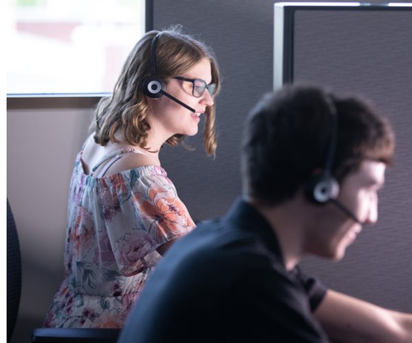 Two people who are visually impaired sitting at their computers with headsets on