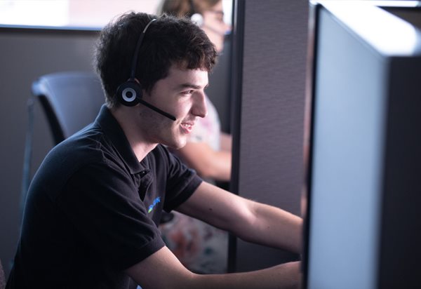 A male employee working is his cubicle in front of his computer and headset